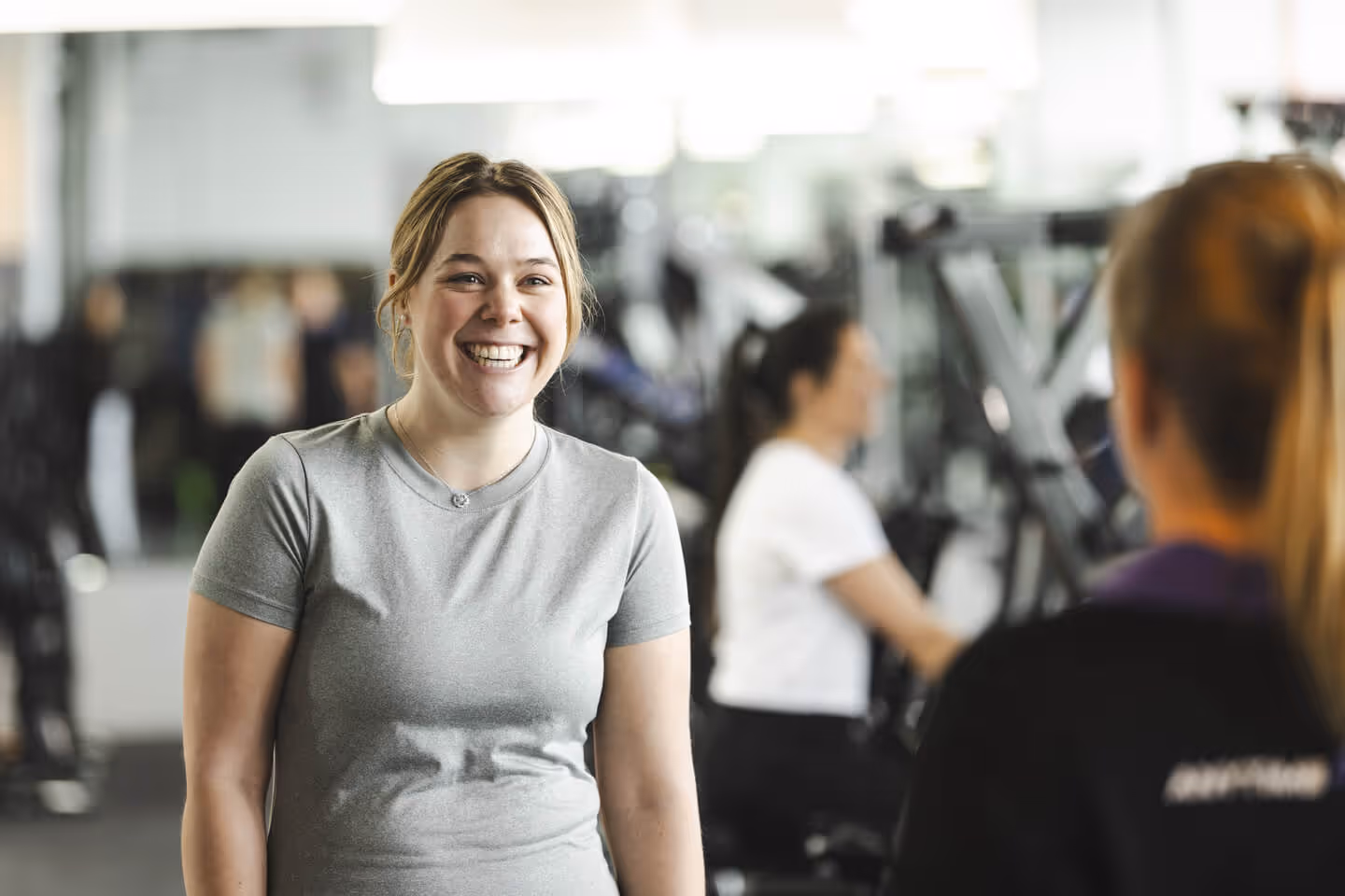 Smiling member talking with an Anytime Fitness trainer in a bright, supportive gym environment.